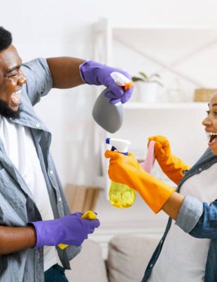 Cleaning Fun. Joyful African Couple Playfully Aiming With Sprayers At Each Other